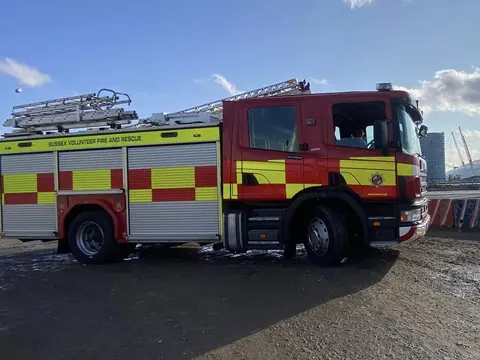 A red and yellow fire appliance parked on hard standing