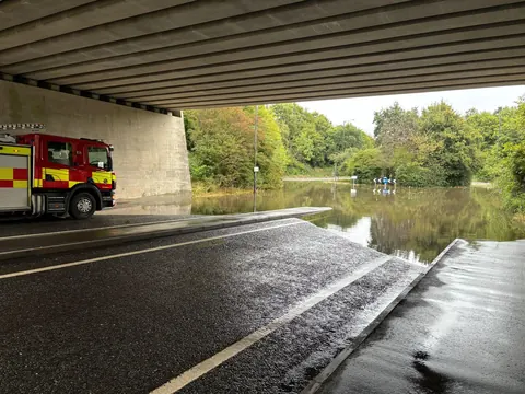 A fire appliance beside a flooded road under a bridge